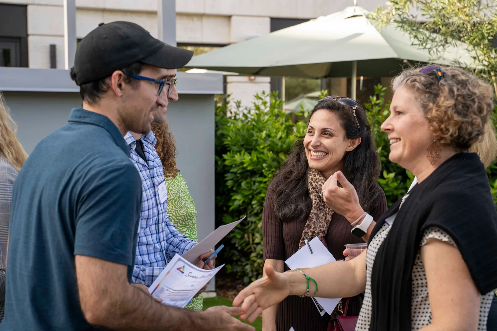 Four guests in animated conversation under a patio umbrella at the 2025 Summer Wine Social