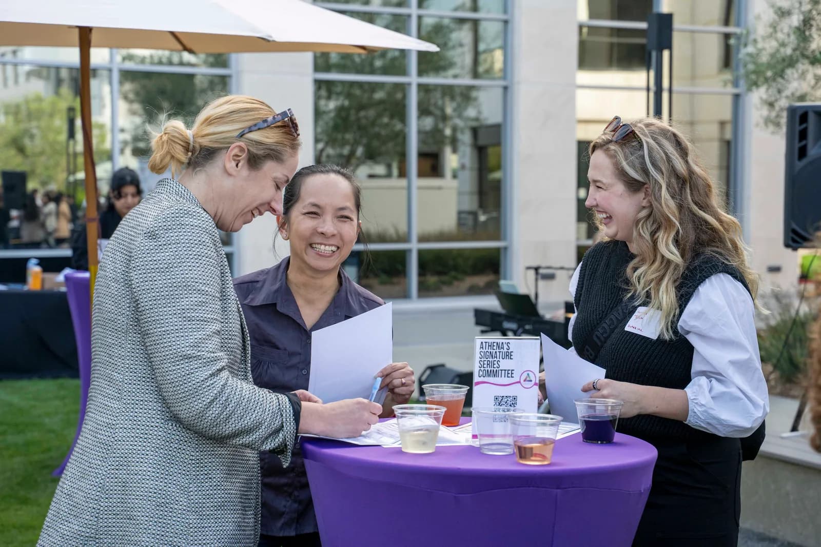 Three attendees signing in at a purple cocktail table at the 2025 Summer Wine Social